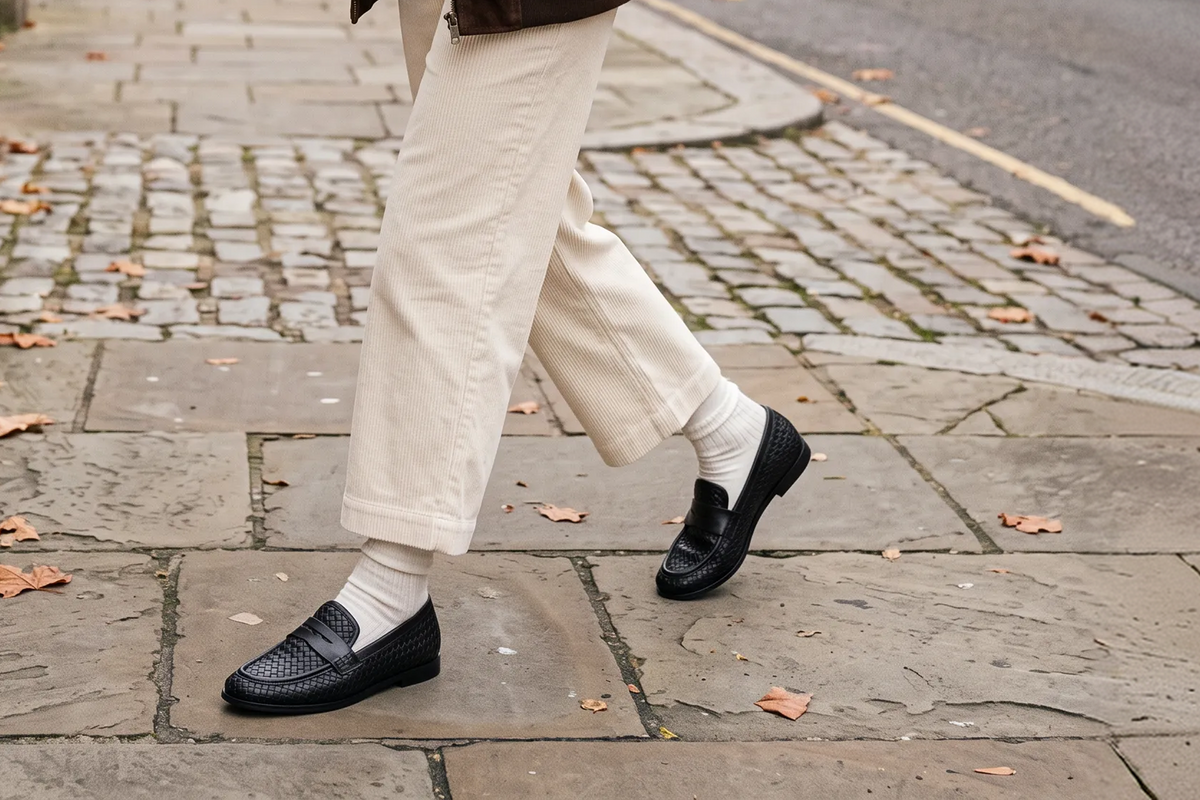 The Clover in black, worn with cream trousers and white socks on a stone pavement.