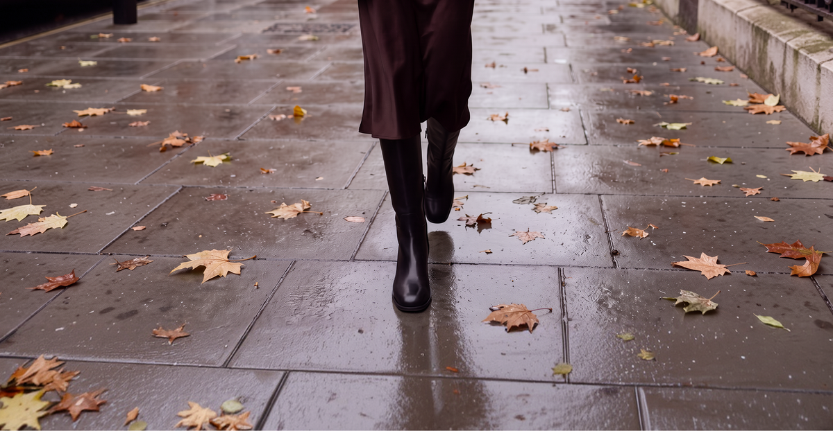 Maple Knee Boot - Black worn with a brown coat on a wet autumn pavement.